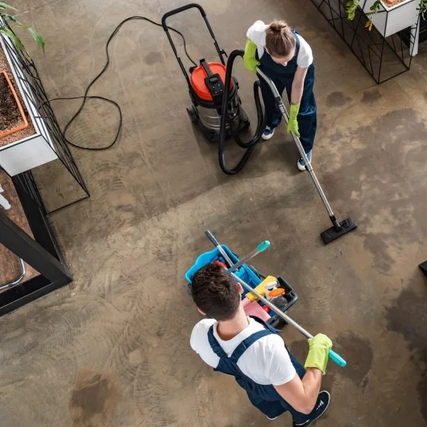 Two cleaners vacuuming and mopping an open-plan office, seen from above