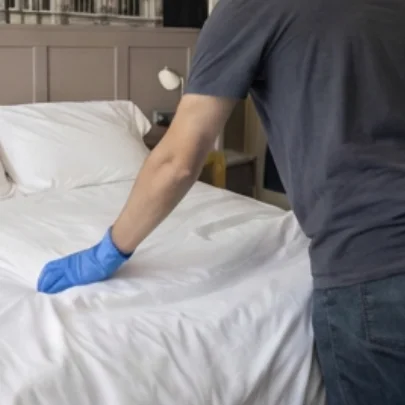 Gloved hand smoothing the sheets of a hotel bed